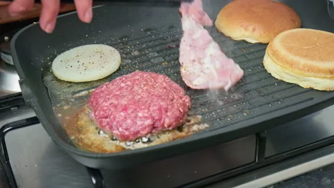 Frying a slice of bacon and burger ingredients on the grill in 4K. Stock Footage 153741098