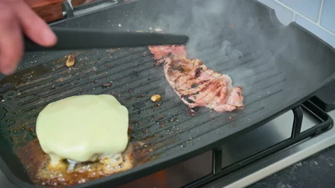 Frying a slice of bacon and burger ingredients on the grill in 4K. Stock Footage 153745907