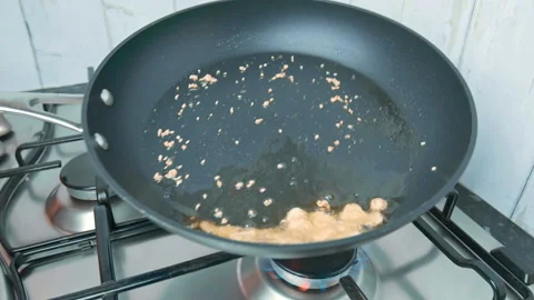 Frying sliced garlic into a pan until golden crisp, making garlic chips in 4K. Stock Footage 141307655