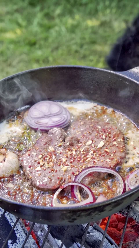 Frying steak in a cast iron pan on the grill. Steak with garlic, onions, thyme. Video stock 315277854