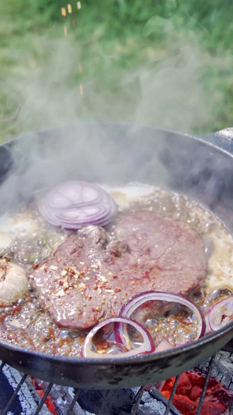 Frying steak in a cast iron pan on the grill. The cook adds spices to the steak. Stock Footage 315277912