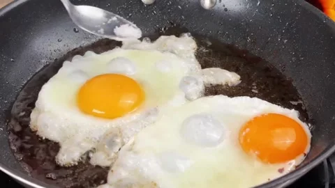 Frying sunny side up eggs in a pan and seasoning with salt for breakfast Stock Footage 325032733
