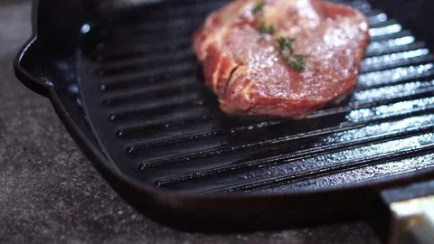Frying thick piece of raw beef steak meat on hot oily grill pan in slow motion Stock Footage 105895116