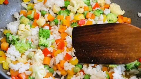 Frying vegetables and rice in a pan at home in a kitchen setting Stock Photos