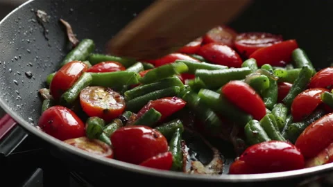Frying vegetables cherry tomatoes green beans onion with oil in pan close up Stock Footage 116104306