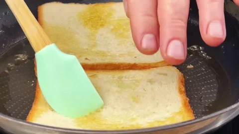 Frying white bread slices in a pan with butter to make a crispy golden toast Stock Footage 324943399