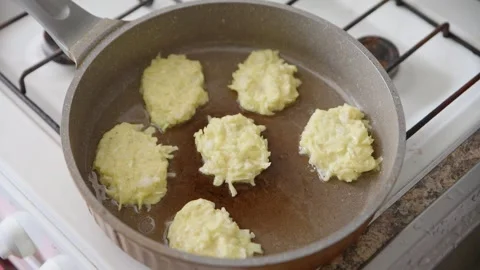 Frying zucchini potato pancakes batch cooking home kitchen stove top view Stock Footage 333698929