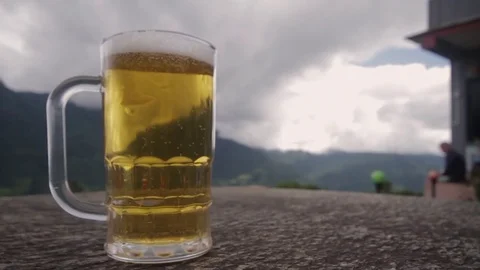 Full Beer Bubbling on Table with Mountains in Background. Close Up Slow Motion. Stock Footage 85296438