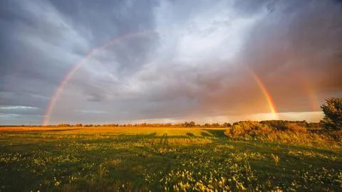 Full double rainbow arcing over a wide green field with yellow wildflowers .. Stock Photos
