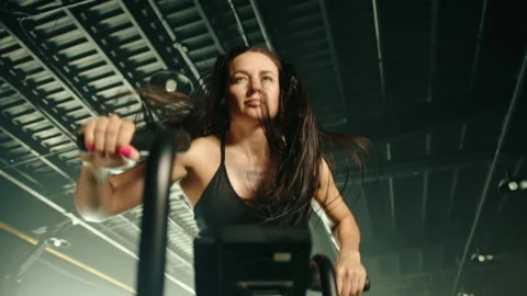 Full face medium close up of woman training on air bike, hair is wind blown Stock Footage 239470020