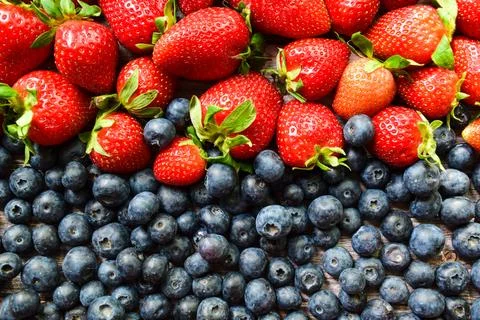 Full frame close-up of fresh ripe red strawberries and dark blueberries arranged Stock Photos