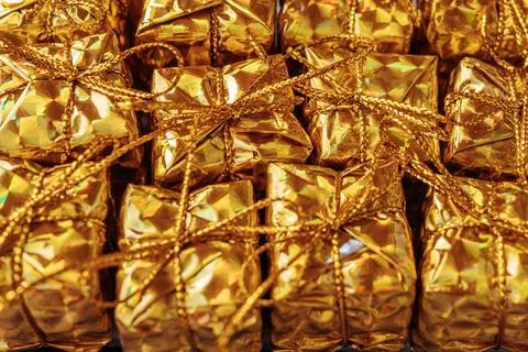 A full-frame close-up of several shiny gold gift boxes tied with gold. Stock Photos