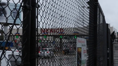 Full HD EXT DAY pan handheld Mexico border behind a fence with walking people Stock Footage 72347999