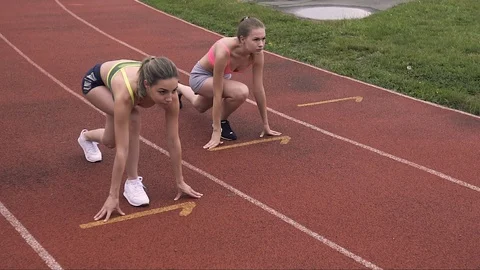 Full leight of two gorgeous female runners in start position on stadium Видео 99153162
