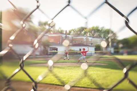 Full length of baseball player throwing ball while playing on field seen through Stock Photos
