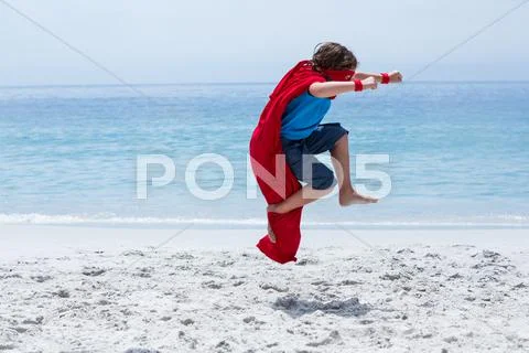 Full length of boy in superhero costume jumping at sea shore Stock Photos