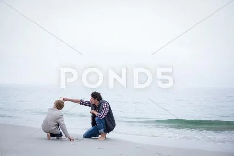 Full length of father pointing while kneeling with son at sea shore Stock Photos