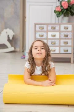 Full length front view cute playful little girl sitting on yoga mat looking Foto stock