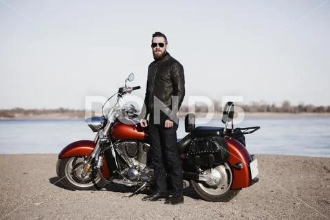Full length portrait of biker standing by motorcycle at lakeshore Stock Photos