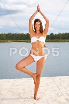 Full-length portrait of a charming tanned girl practicing yoga on the beach Stock Photos