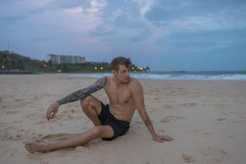Full-length portrait of handsome caucasian man sitting on the sand on the bea Stock Photos