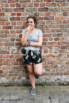 Full length portrait of young adult woman covering her mouth leaning again.. Stock Photos