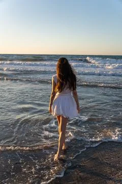 Full length rear view of young woman walking barefoot in sea foam on Crete .. Stock Photos