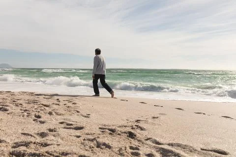 Full length of retired biracial senior man walking on shore at beach during Stock Photos