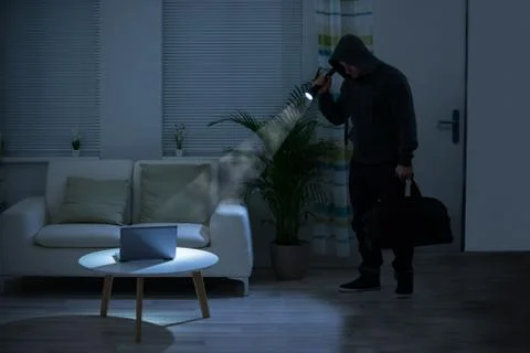 Full length of robber holding flashlight over laptop on table at home Stock Photos