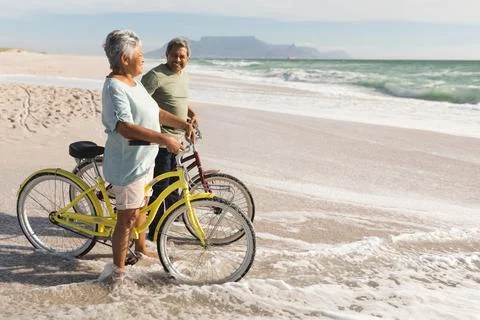 Full length of senior multiracial couple with bicycles standing on shore at Stock Photos