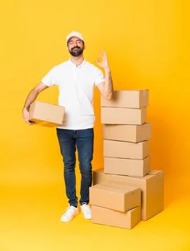 Full-length shot of delivery man among boxes over isolated yellow background  Stock Photos