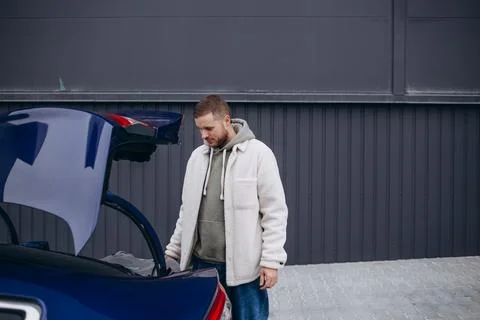 Full length side view of young businessman looking in car trunk at countrysid Stock Photos