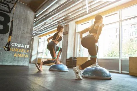 Full length of two young athletic women in sportswear squatting and exercising Stock Photos
