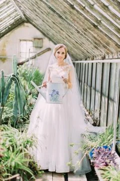 Full-length view of the smiling bride holding the watering can in the greenhouse Stock Photos
