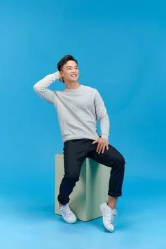 Full length view of young man in jeans and gray t-shirt sitting cube on blu.. Stock Photos
