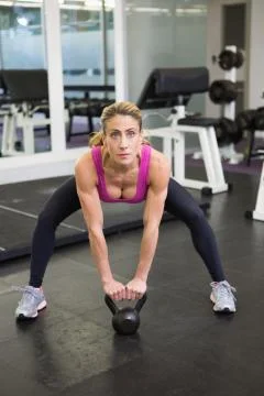 Full length of woman lifting kettle bell in gym Stock Photos