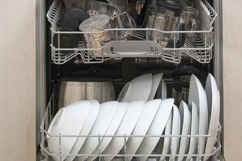 Full loaded Dishwasher machine. Integrated Dishwasher with white plates front Stock Photos