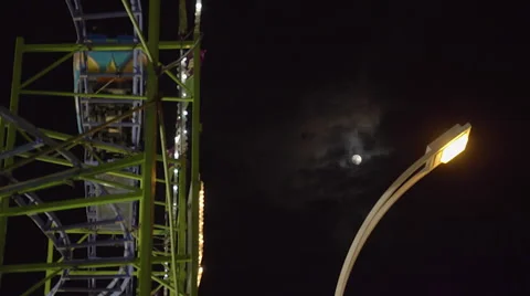 Full moon behind clouds at Amusement park as roller coaster passes by. 4K UHD Stock Footage 54304815