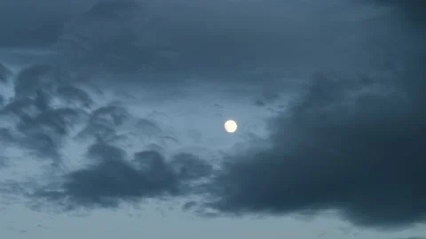 A full moon can be seen through moving clouds at blue hour. Vídeo Stock 156146372