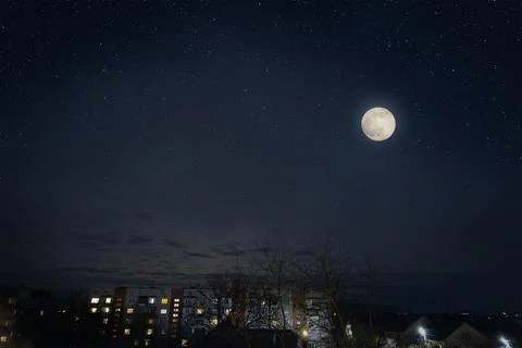 Full moon in dark star sky over town roofs. Stock Photos