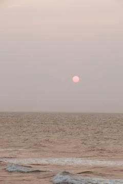 A full moon emerges on the horizon as waves break on the sea's surface Stock Photos