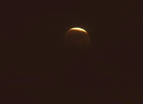 A full moon mostly covered by Earths shadow during a lunar eclipse against a Fotos Stock