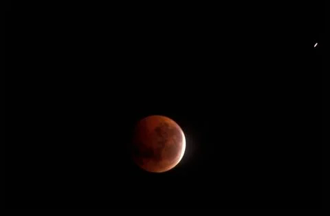 A full moon mostly covered by Earths shadow during a lunar eclipse against a Fotos Stock