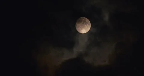 A full moon partially obscured by dark, wispy clouds in the night sky, creating Vídeo Stock 293328687