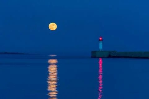 Full moon reflected next to the lighthouse in the water of the port of Almeri Stock Photos