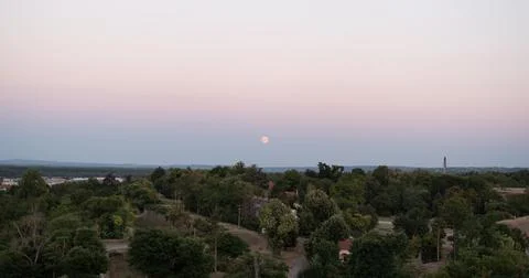 Full moon rises over a dense green forest canopy during twilight Stock Photos