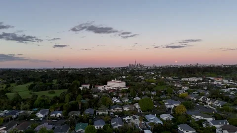 Full moon rises over faint Auckland skyline at dusk, suburban rooftops and tall Stock-Footage 343365001