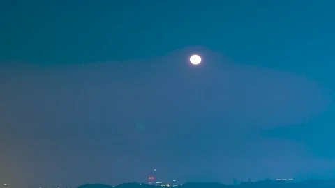 Full moon rising over a distant urban skyline at blue hour twilight 스톡 동영상 341995965