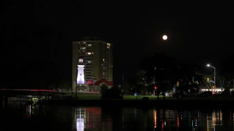 Full moon rising over lighthouse time lapse - river reflects light, cars drive Video stock 319973740