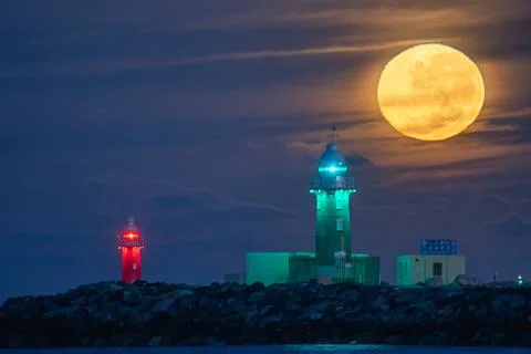 Full moon setting behind green lighthouse at dawn Photos